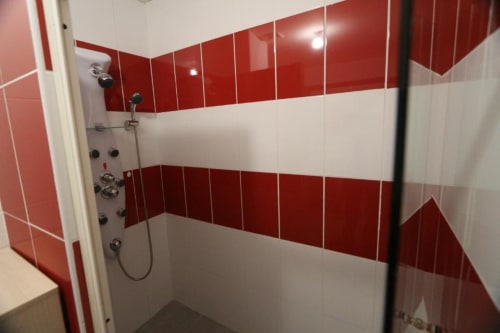 Modern bathroom with red and white striped tile walls and glass shower enclosure at Appart'Hôtel villa in Cholet