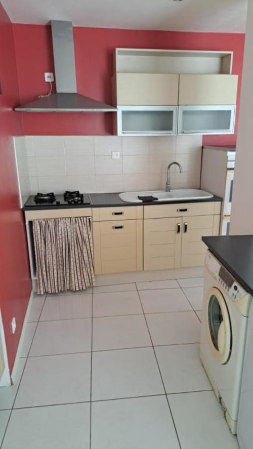 Modern kitchenette with cream cabinets, black countertop, gas stove, sink, and washing machine in Appart'Hôtel villa, Cholet