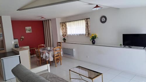 Open-plan living area in Cholet villa with dining table, TV, red accent wall, and garden view windows