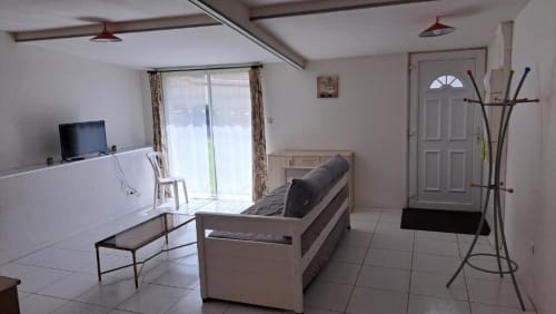 Bright villa living room at Appart'Hôtel Cholet with sofa, TV, kitchenette, and garden view through patio doors