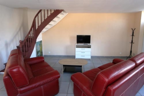 Spacieux séjour de l'Appart'Hôtel villa avec canapés en cuir rouge, TV écran plat, escalier en bois et carrelage