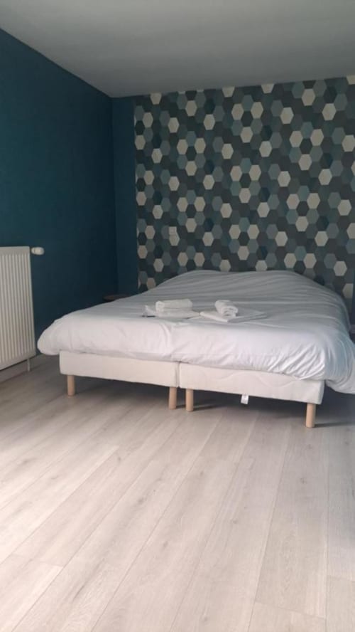 Chambre moderne à l'Appart'Hôtel Cholet : murs bleu-vert, papier peint motif hexagonal, lit blanc pieds bois et luminaire