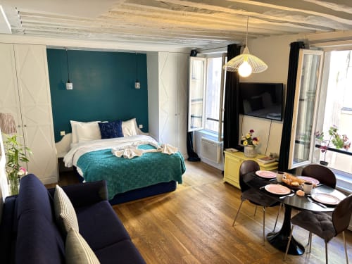 Estudio moderno en París con pared acentuada en azul verdoso, cama queen, zona de comedor y vistas al jardín cerca del Louvre