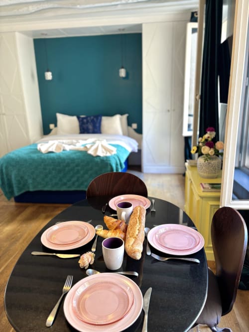 Área de comedor del apartamento parisino ALDARO con mesa elegantemente decorada, dormitorio con pared de acento color verde azulado visible, vista al jardín