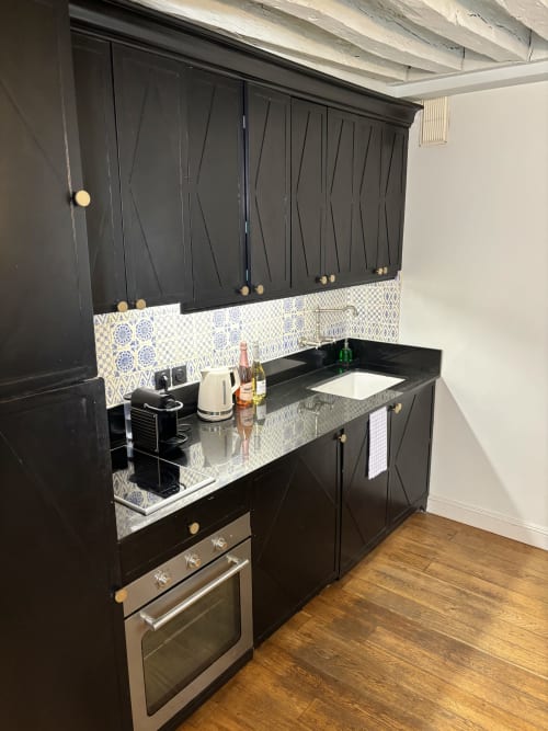 Cocina moderna negra parisina con azulejos estampados, encimera cuarzo blanco, horno acero inoxidable y herrajes latón