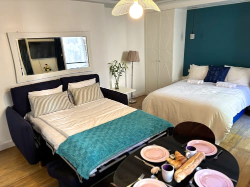Estudio moderno en París con sofá cama, segunda cama, pared acentuada en azul verdoso y desayuno cerca del Louvre