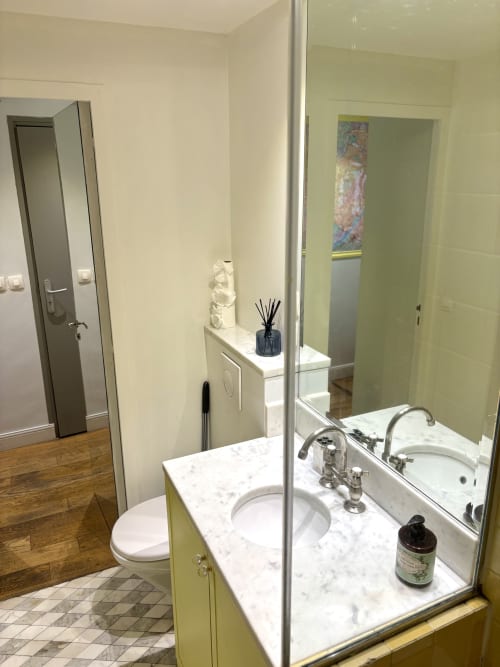 Baño moderno con encimera de mármol, lavabo blanco y espejo en un apartamento parisino cerca del Louvre