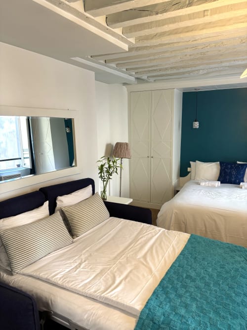 Dormitorio con dos camas en apartamento parisino moderno, vigas vistas, pared de acento turquesa y ventana con vista al jardín en el hotel ALDARO