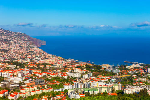 Vista aérea de Funchal, Madeira com edifícios coloridos em cascata descendo a encosta em direção ao oceano turquesa e porto