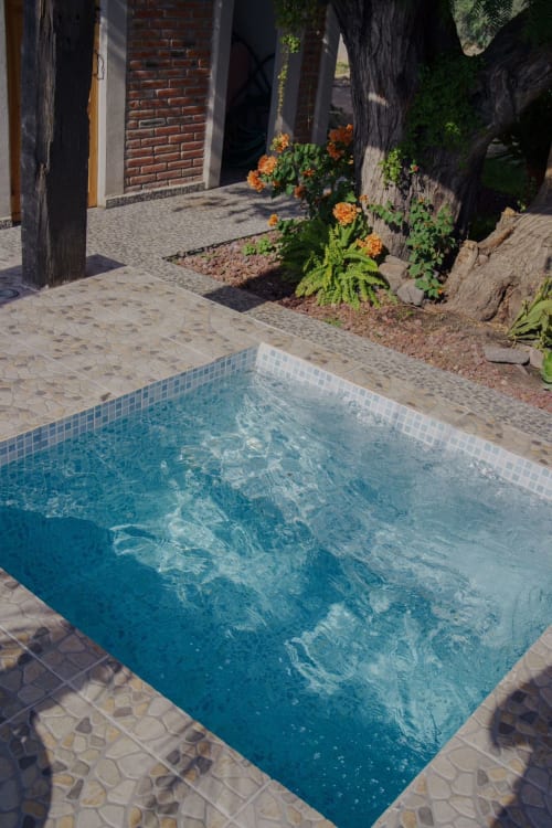 Pequeña piscina rectangular con agua turquesa en patio de villa del Hotel El Porvenir, rodeada de terraza de piedra y flores
