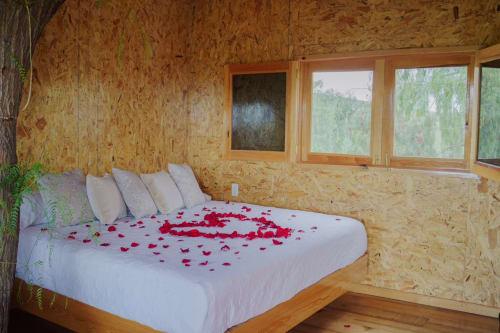 Dormitorio romántico en villa Hotel El Porvenir con pétalos de rosa en cama blanca, paredes de corcho, marcos de madera y vistas al jardín