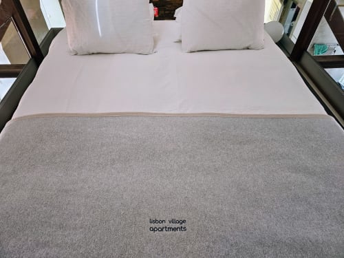 Quarto moderno no Lisbon Village Apartments com almofadas brancas, roupa de cama rosa e manta cinzenta em Lisboa