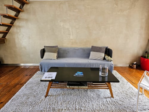 Espaço de estar em loft moderno de Lisboa com sofá cinzento, mesa de centro em madeira e vista da cidade contra paredes texturizadas