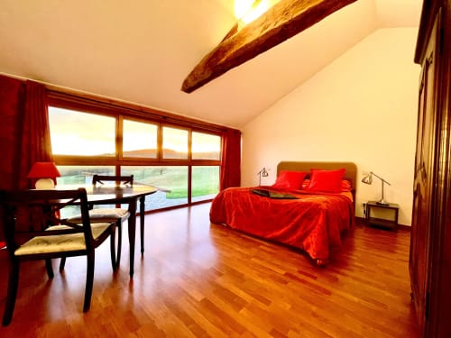 Spacious bedroom at Domaine Joseph Lafarge Wine Resort in Lugny with red bedding, wooden beams, and garden views