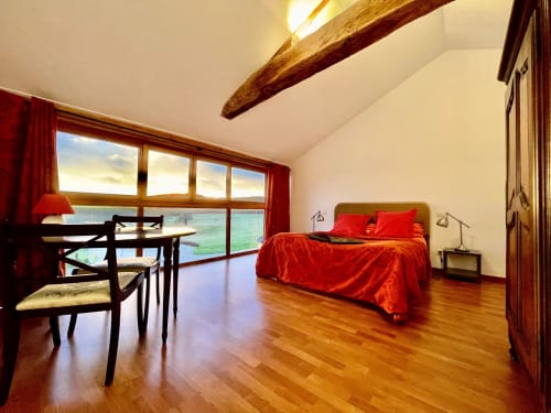 Chambre lumineuse au Domaine Joseph Lafarge Wine Resort à Lugny avec literie rouge, poutres en bois, vue sur le jardin et parquet