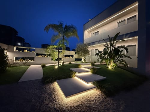 Eich Business Accommodation night courtyard with illuminated pathways, palm tree, and modern white building in Santa Maria