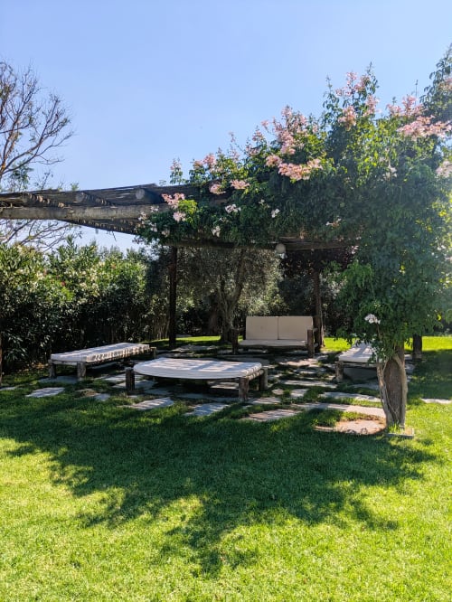 Rustic garden lounge at Casas de Juromenha with wooden pergola, seating, pink flowers and green lawn