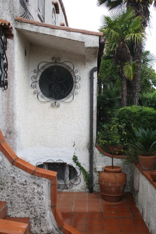 Cortile rustico a Myob Roma con finestra in ferro battuto, vasi in terracotta e lussureggianti palme