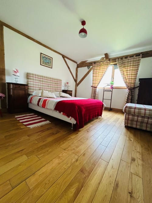 Chambre spacieuse avec poutres en bois, literie écossaise rouge, rideaux à carreaux et parquet à La Conciergerie des