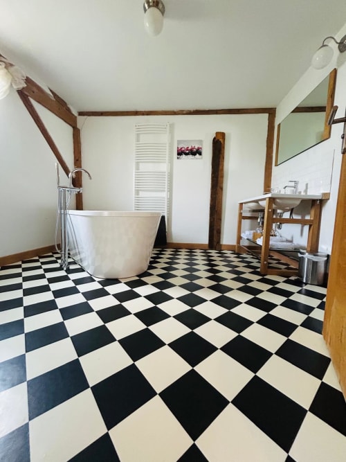 Salle de bains spacieuse au charme cottage, sol damier noir et blanc, baignoire de relaxation, meuble vasque bois et porte-serviettes chauffant