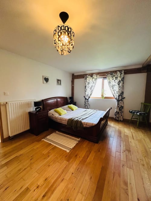 Chambre spacieuse à la Conciergerie des Lacs à Gérardmer avec parquet, lit en bois foncé et vue sur le jardin