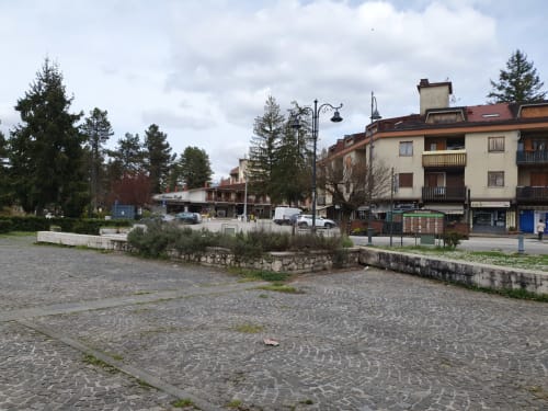 Piazza principale di Roma con edifici storici, lampione e alberi sotto cielo nuvolato