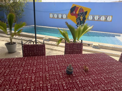 Salon au bord de la piscine de Keur Medzo avec décor d'inspiration africaine, art mural bleu et palmiers surplombant la piscine turquoise