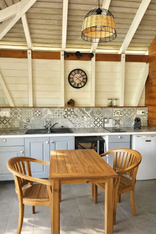 Modern cottage kitchen at Cottages du Lagon with wooden dining table, white cabinetry, and decorative tile backsplash