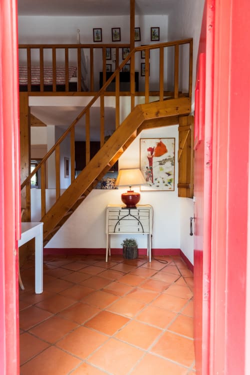 Entrada iluminada da villa Casas de Juromenha com escada de madeira, azulejos de terracota e moldura de porta rosa néon