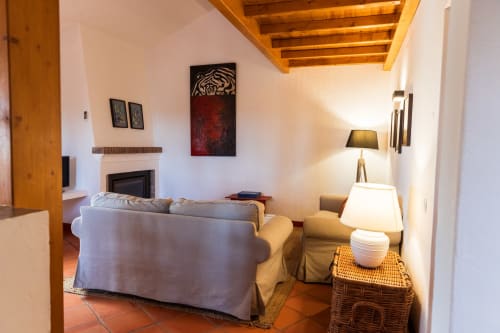 Aconchegante sala de estar na villa Casas de Juromenha com lareira, mobiliário confortável, vigas de madeira e iluminação quente