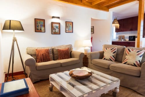 Aconchegante sala de estar na villa Casas de Juromenha com sofás bege, vigas de madeira, arte emoldurada e vista aberta para a cozinha