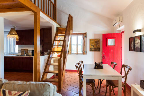 Interior espaçoso de villa em Casas de Juromenha com escadas de madeira, mesa de jantar, porta vermelha e cozinha aberta em Juromenha,