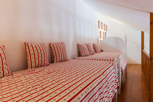 Quarto brilhante na villa Casas de Juromenha com roupa de cama listrada em vermelho e creme, almofadas decorativas e piso de madeira