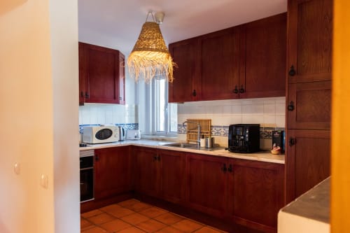 Cozinha moderna na vila Casa 1 de Casas de Juromenha com marcenaria borgonha, luminária pendente trançada e design contemporâneo