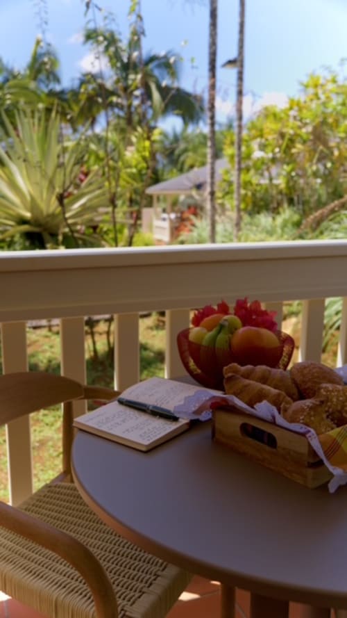Petit-déjeuner tropical à Forty Palms : corbeille de fruits, viennoiseries et carnet sur une terrasse avec vue sur les palmiers luxuriants