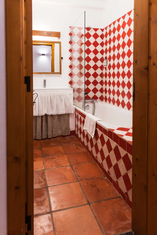 Banheiro em Casas de Juromenha com azulejos losango vermelho e branco, piso de terracota e batente de porta de madeira