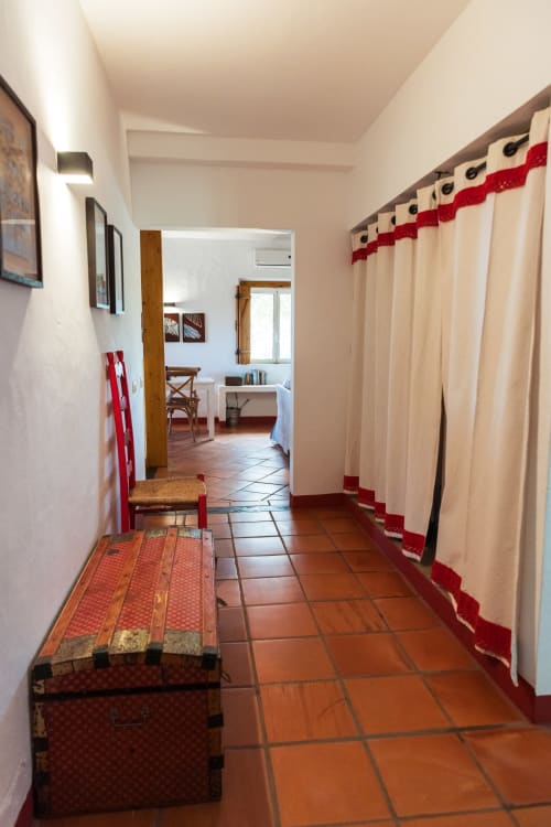 Corredor da villa Casa 1 em Casas de Juromenha com azulejos de terracota, cortinas creme com detalhe vermelho e acesso aos quartos de hóspedes