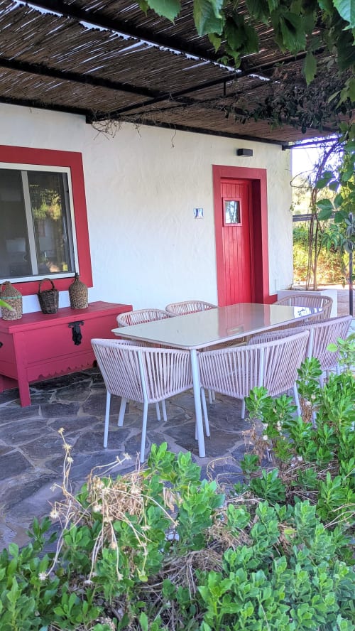 Pátio externo da villa Casas de Juromenha com mesa de jantar, acentos vermelhos e videiras trepadeiras acima