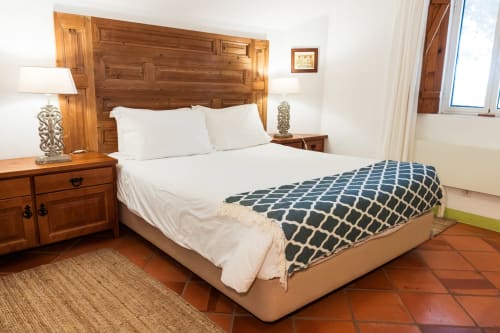 Quarto espaçoso na villa Casas de Juromenha com cabeceira de madeira, roupa de cama branca, manta azul estampada e azulejos de barro