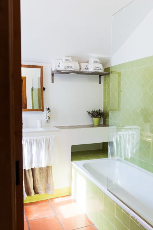 Banheiro moderno na villa Casas de Juromenha com paredes de azulejos verdes, pia branca, banheira e acessórios contemporâneos