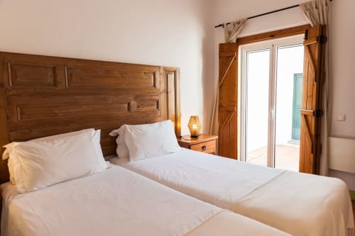 Quarto brilhante com cama de madeira, roupas de cama brancas e vista para o terraço na villa Casas de Juromenha, Portugal