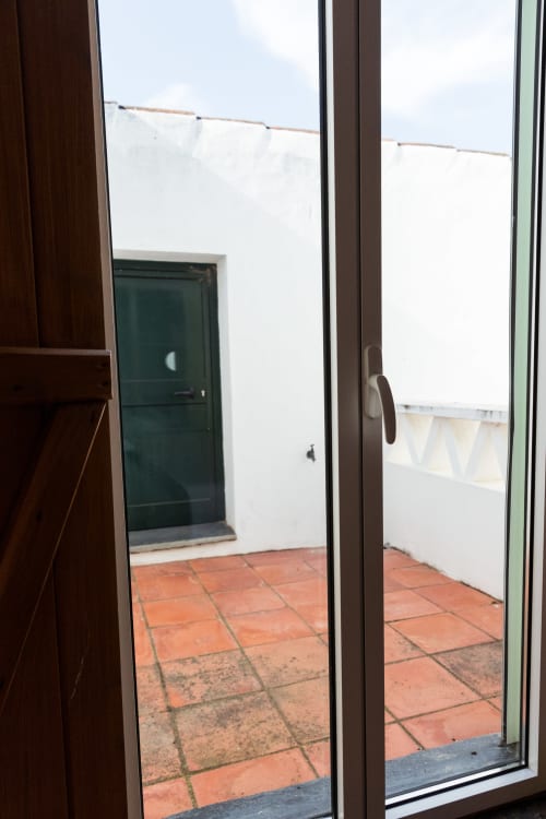 Vista da villa Casas de Juromenha para o terraço com azulejos laranja, paredes brancas e porta verde em Juromenha, Portugal