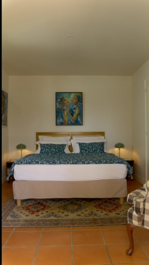 Chambre du cottage FORTY PALMS en Guadeloupe avec lit en bois, literie motif turquoise, sol en terre cuite et vue sur le jardin