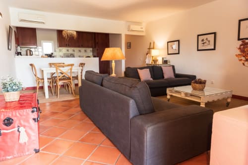 Espaçosa sala de estar na villa Casas de Juromenha com sofás escuros, área de refeições, piso em terracota e iluminação aconchegante