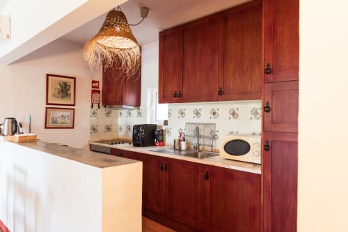 Cozinha moderna com armários em madeira vermelha, azulejos florais e luminária de vime em villa em Casas de Juromenha