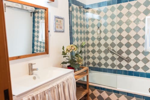 Banheiro elegante na villa Casas de Juromenha com azulejos em padrão diamante azul, pia branca, espelho com moldura de madeira e