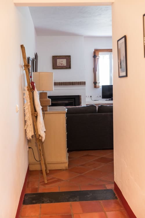 Corredor de entrada da villa Casa 3 em Casas de Juromenha com piso de azulejos de terracota, levando à sala de estar com sofá preto