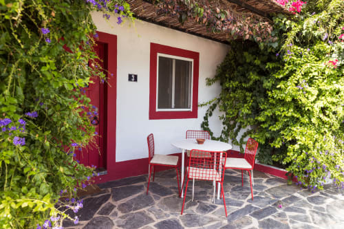 Pátio da Casa 3 em Casas de Juromenha com cadeiras vermelhas, mesa branca, videiras floridas e charmosa arquitetura rústica