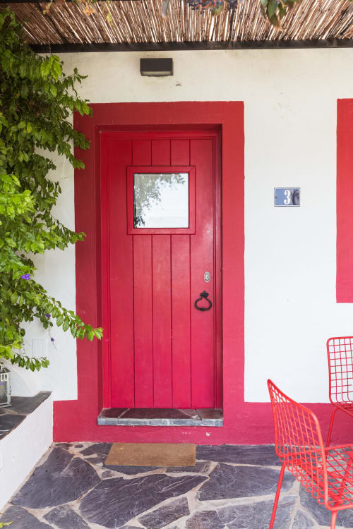Entrada com porta vermelha na Casa 3, vila Casas de Juromenha em Juromenha, com hera verde trepadeira e cadeiras vermelhas no pátio de padrões