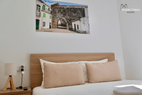 Quarto moderno em Misericórdia Rooms, Guarda com cabeceira em madeira, almofadas bege e fotografia de arquitetura histórica acima da cama